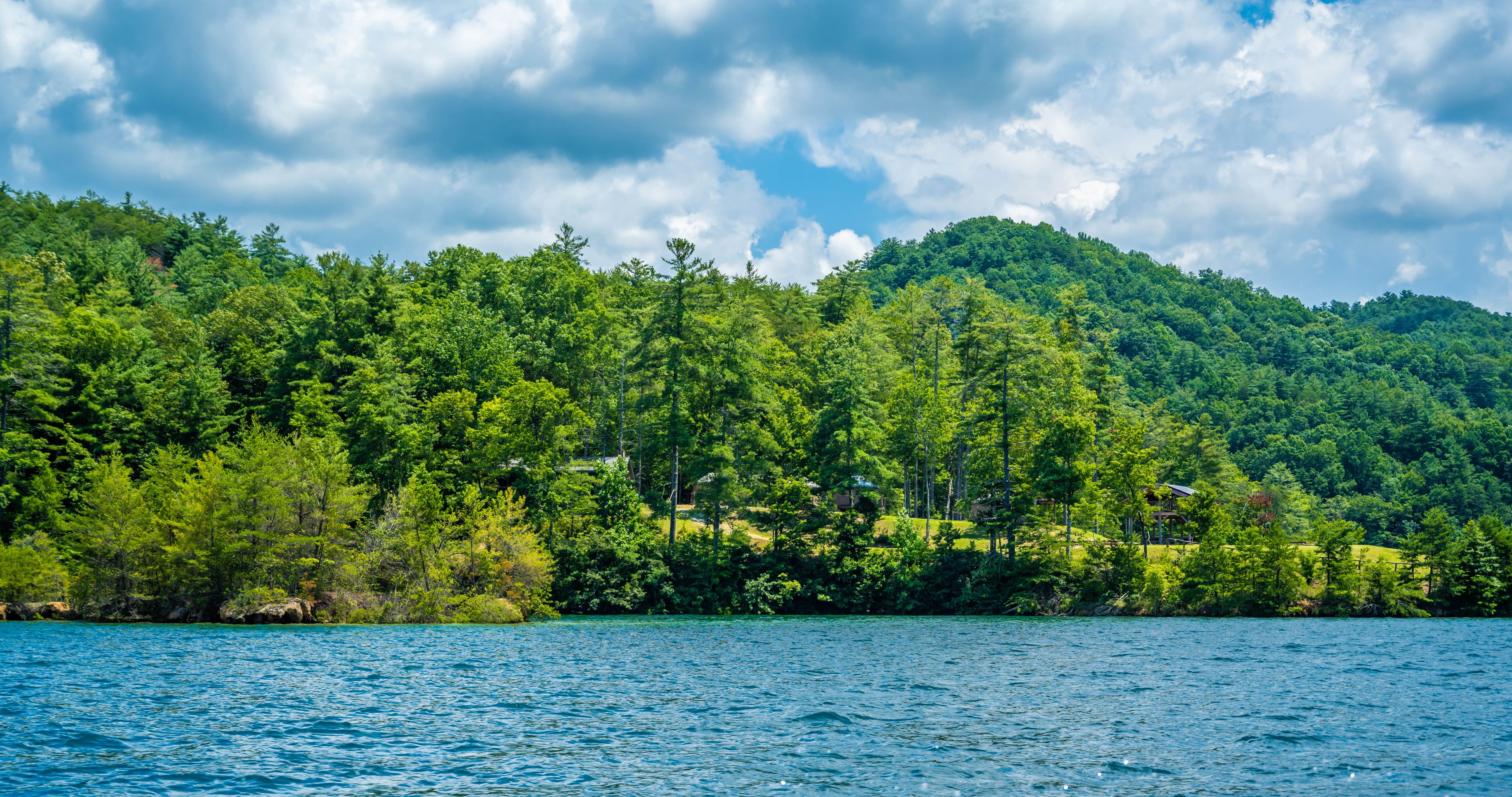 Un lac entouré d’une forêt verdoyante et dense, et une colline sur laquelle se trouve un petit bâtiment.