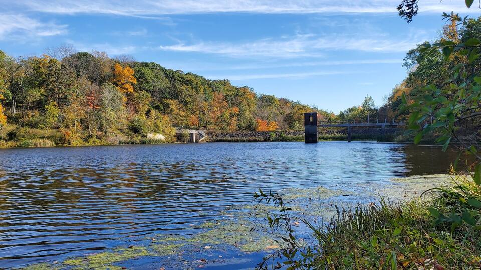 A calm river with a bridge, surrounded by autumn-colored trees.