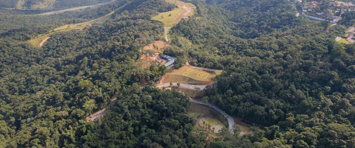 An aerial view of a forested valley with winding roads and a small settlement.