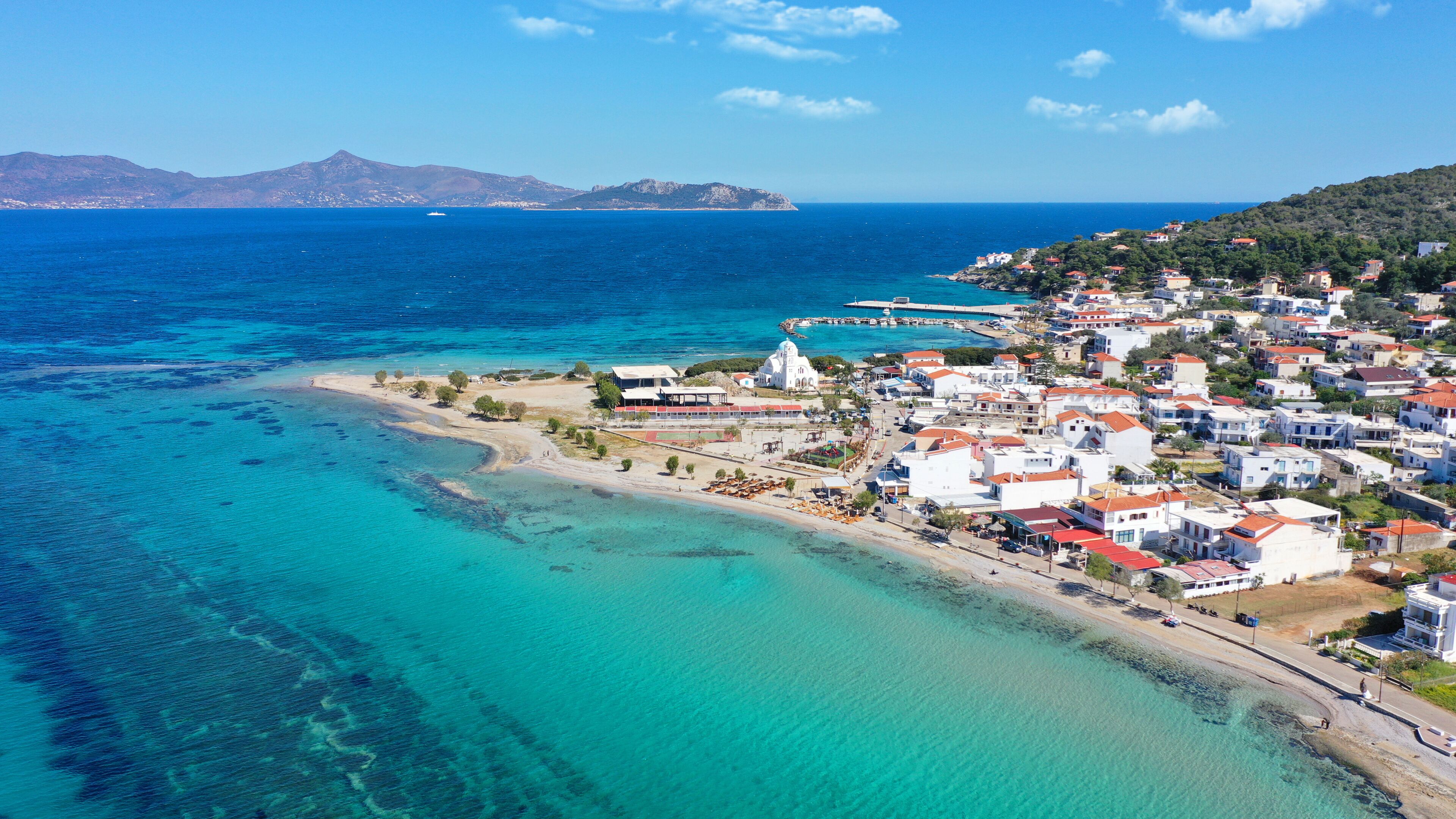 Aerial drone photo of iconic picturesque village, main port and beautiful turquoise beaches of Skala featuring landmark church of Agioi Anargiroi, Agistri island, Saronic gulf, Greece