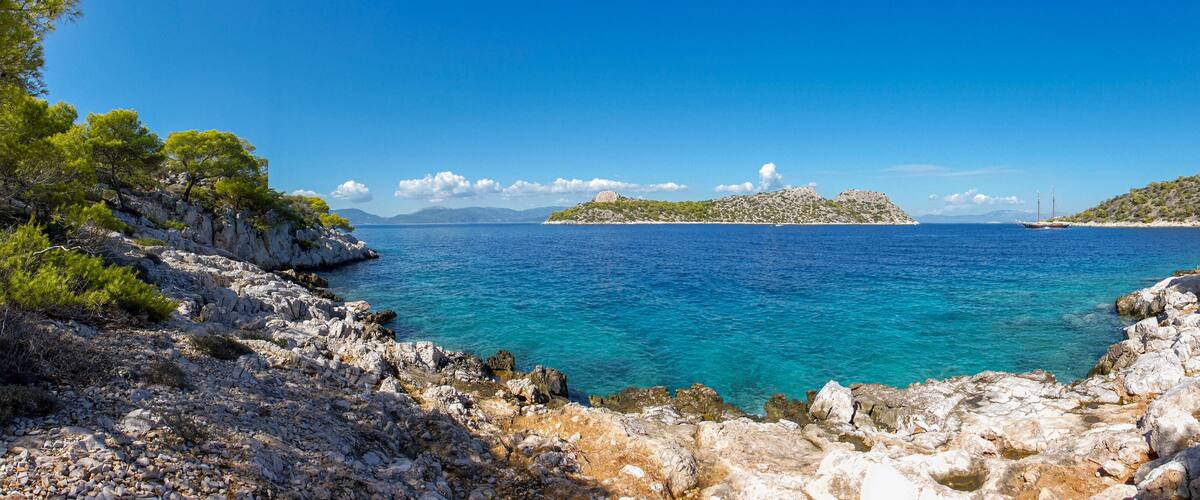 A rocky coastline with clear turquoise waters, a small island with a lighthouse, and lush green trees.
