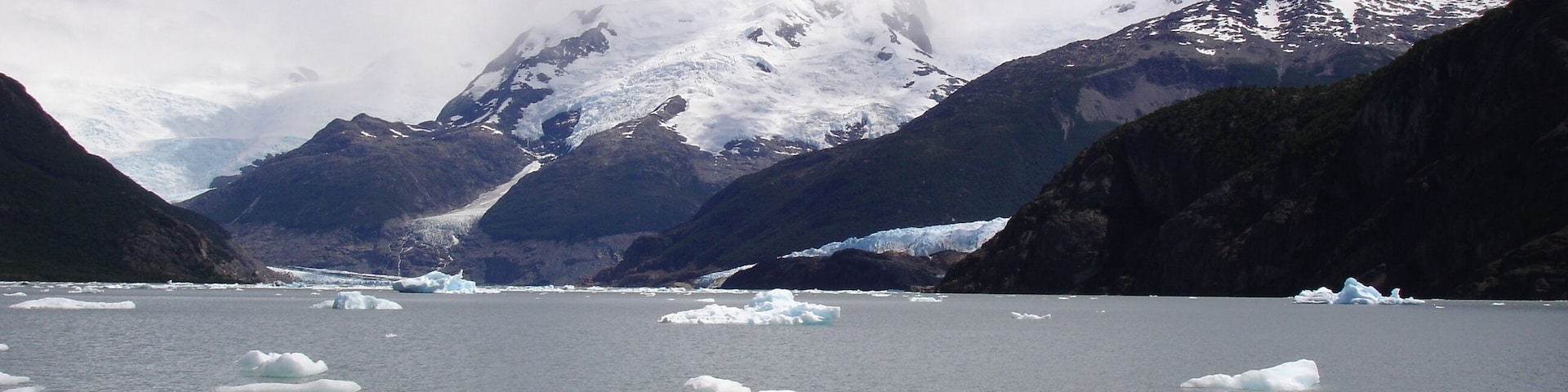 A glacier with icebergs in a fjord surrounded by mountains.