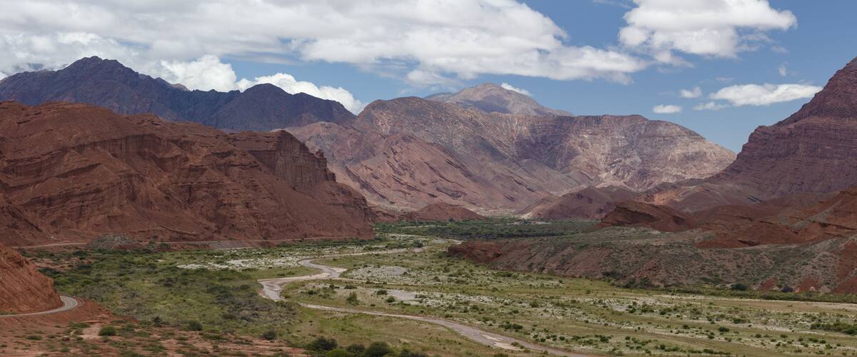 A winding road through a canyon with red rock formations and green vegetation.