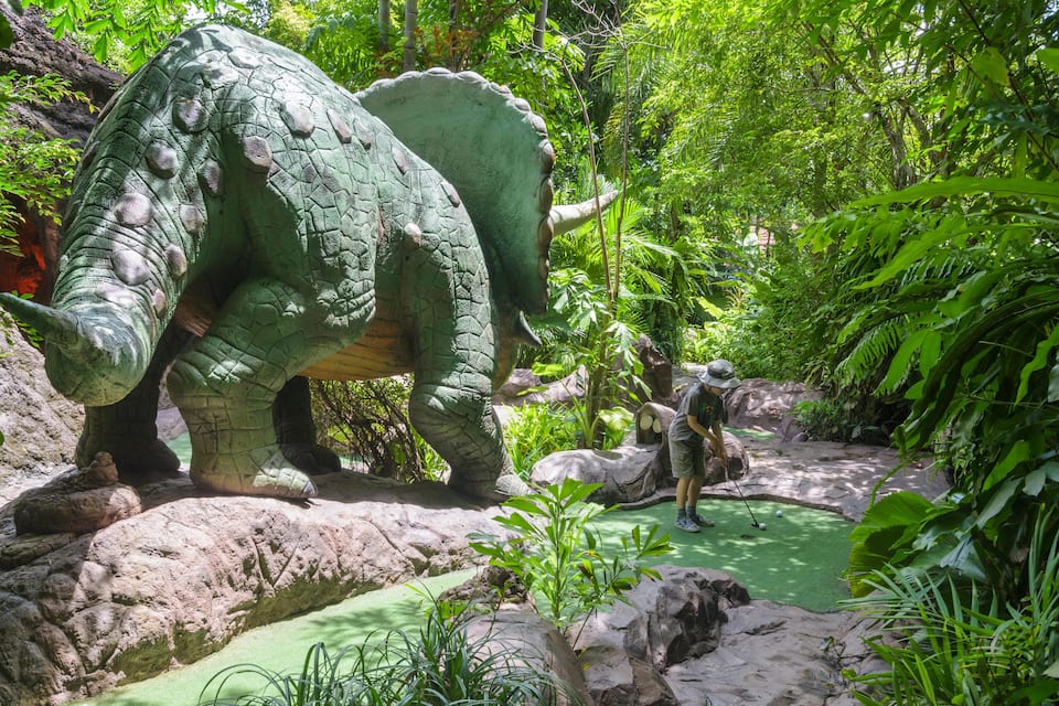 Uma grande estátua de dinossauro verde em meio a uma floresta exuberante.