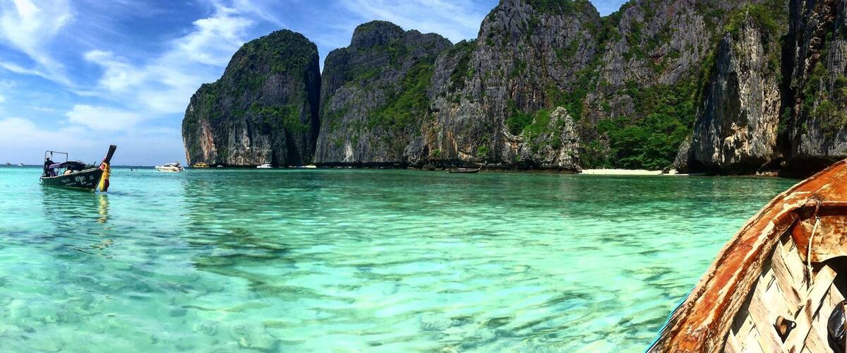 A boat on clear turquoise water with rocky cliffs in the background.