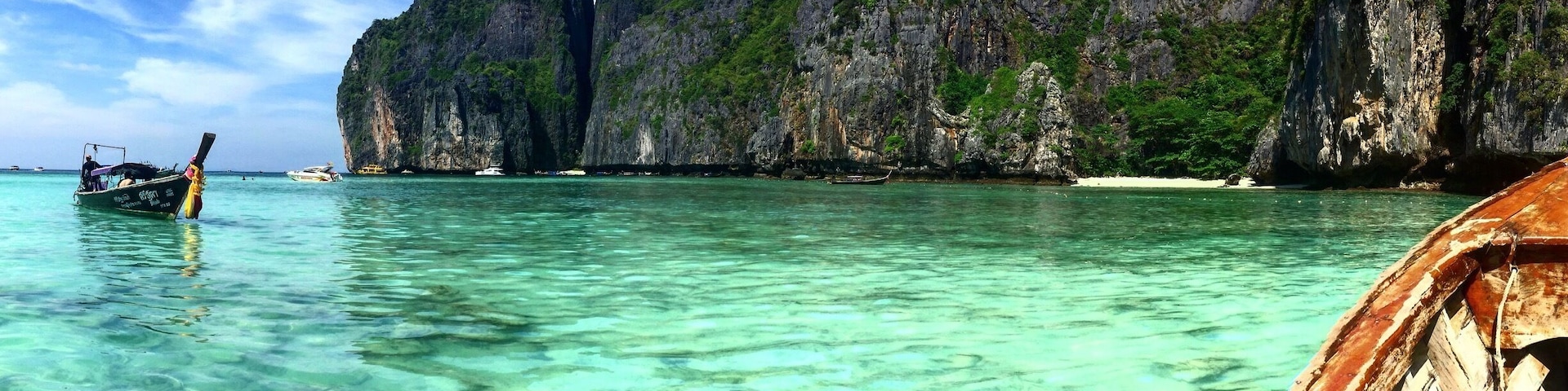 A boat on clear turquoise water with rocky cliffs in the background.