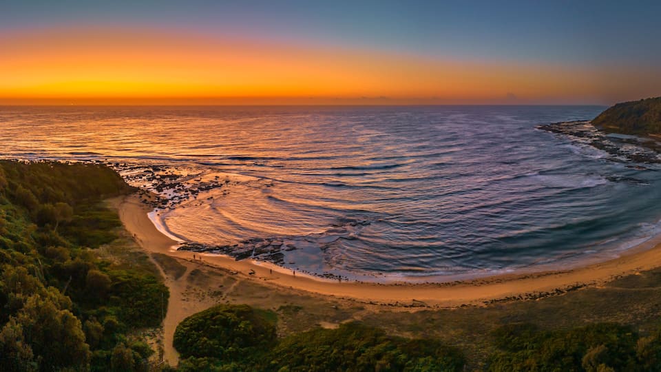 A coastal landscape with a beach, ocean waves, and a forested hill.