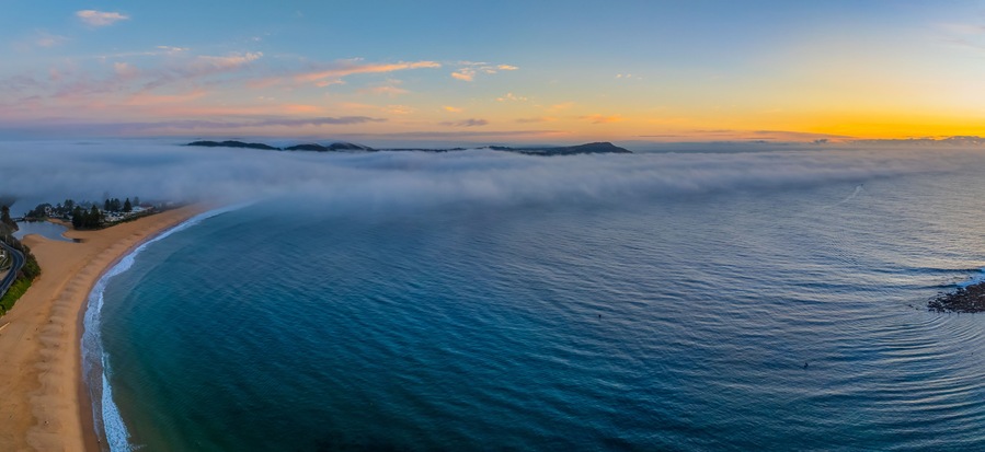 A coastal landscape with a beach, ocean, and a mountain range in the distance.