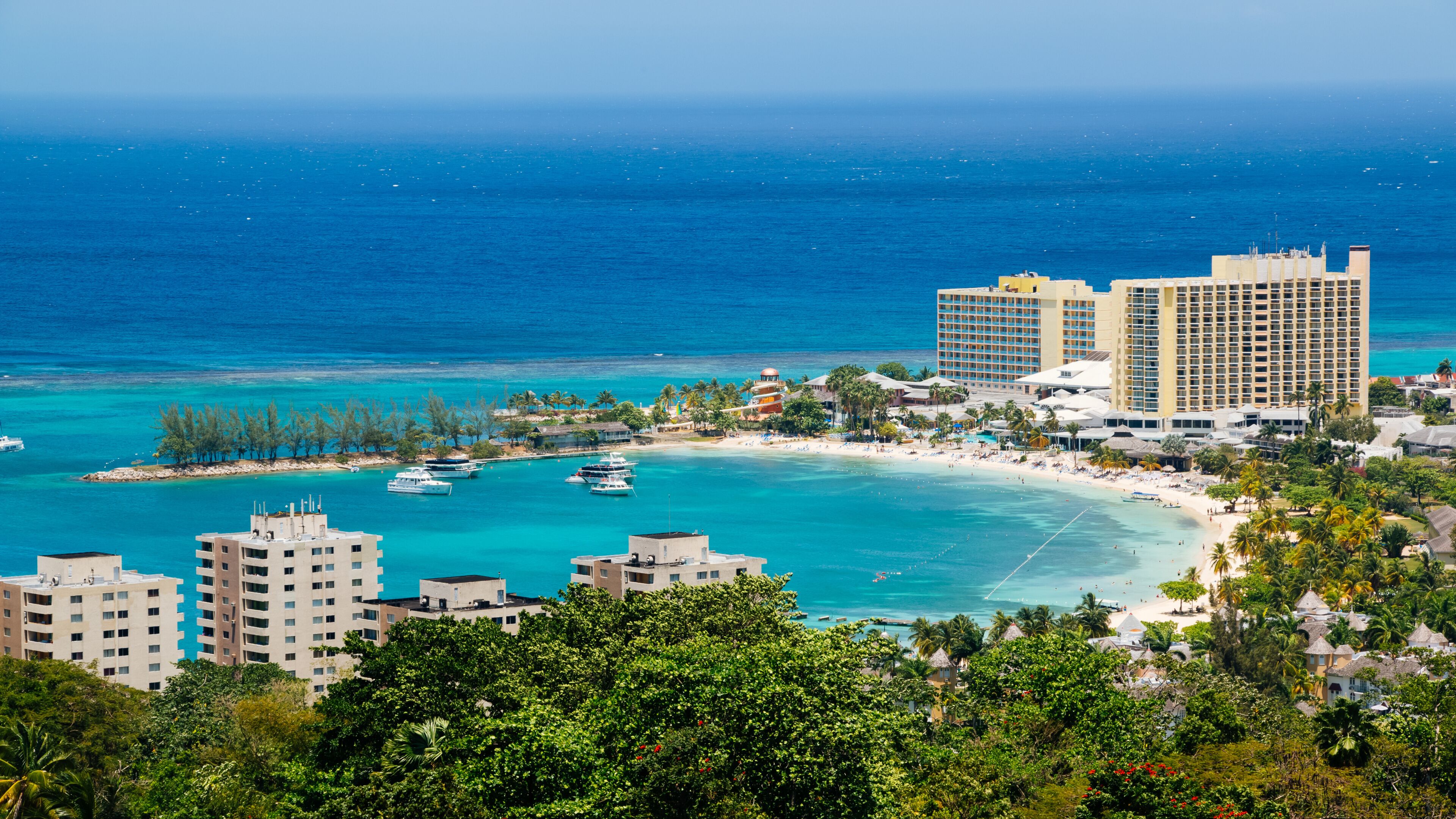 Um resort costeiro com praia, águas turquesa e vários iates.