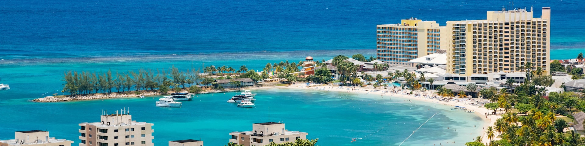 Um resort costeiro com praia, águas turquesa e vários iates.