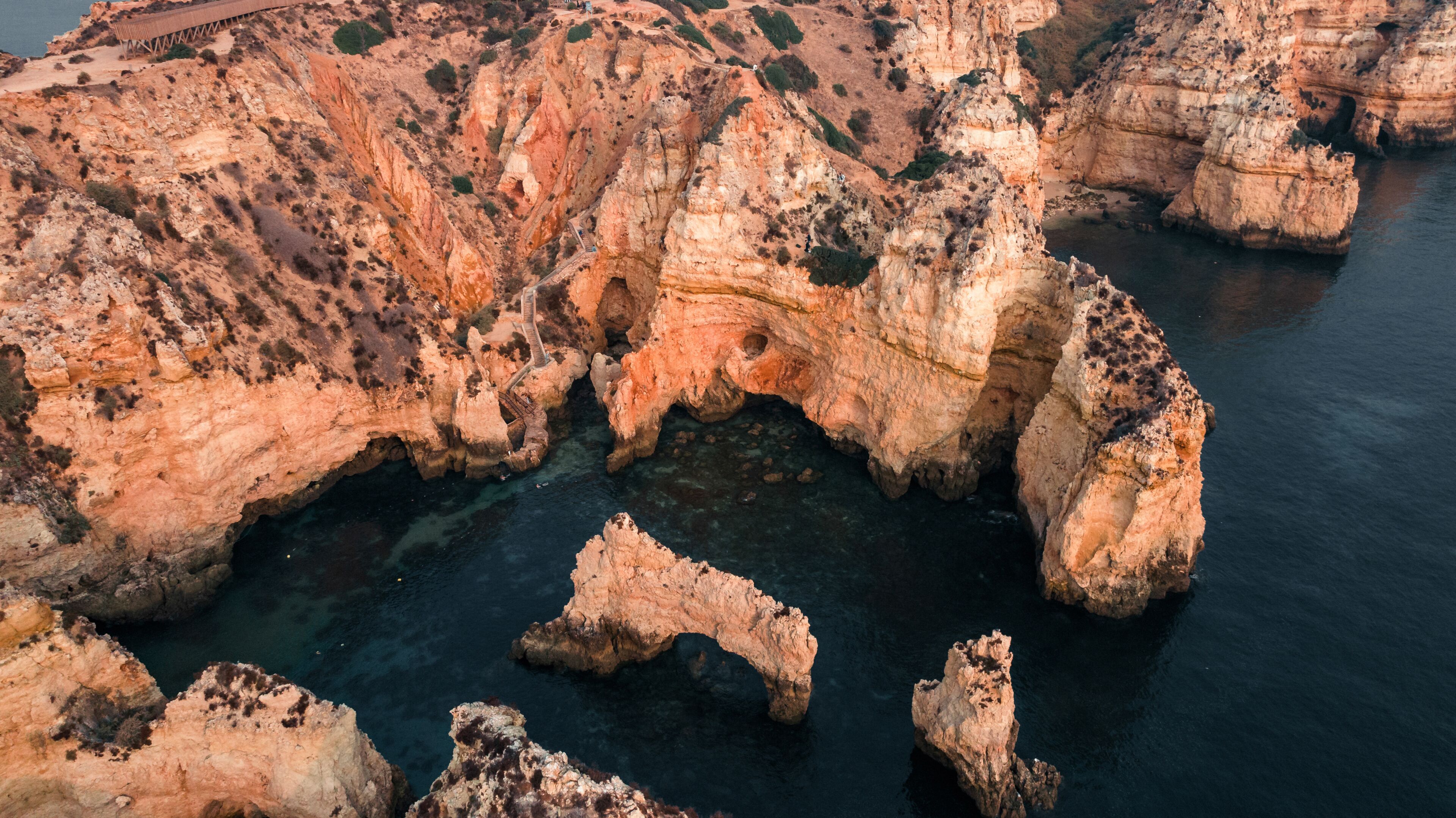 Aerial view of rugged cliffs meeting the tranquil sea, a dance of warm sandstone hues against the cool, deep blue, Lagos, Faro District, Portugal.