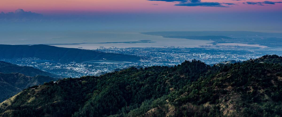 Un paysage urbain côtier, avec des montagnes au premier plan et un ciel au coucher du soleil.