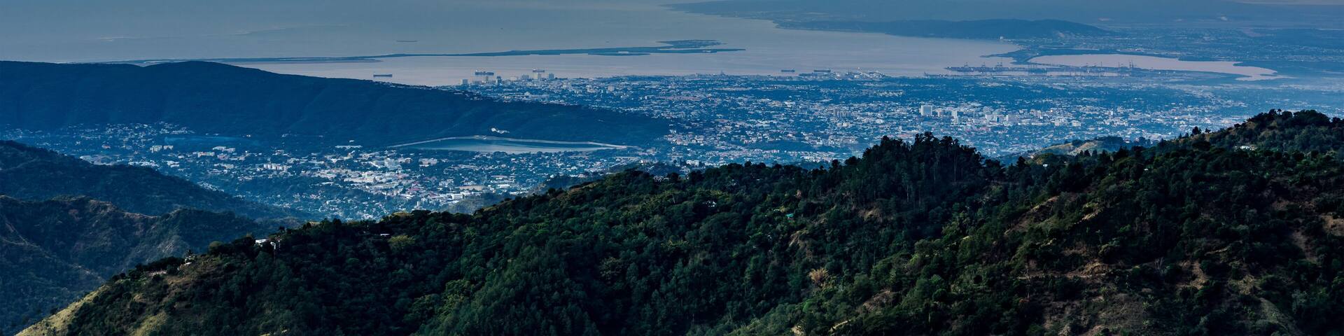A coastal cityscape with mountains in the foreground and a sunset sky.