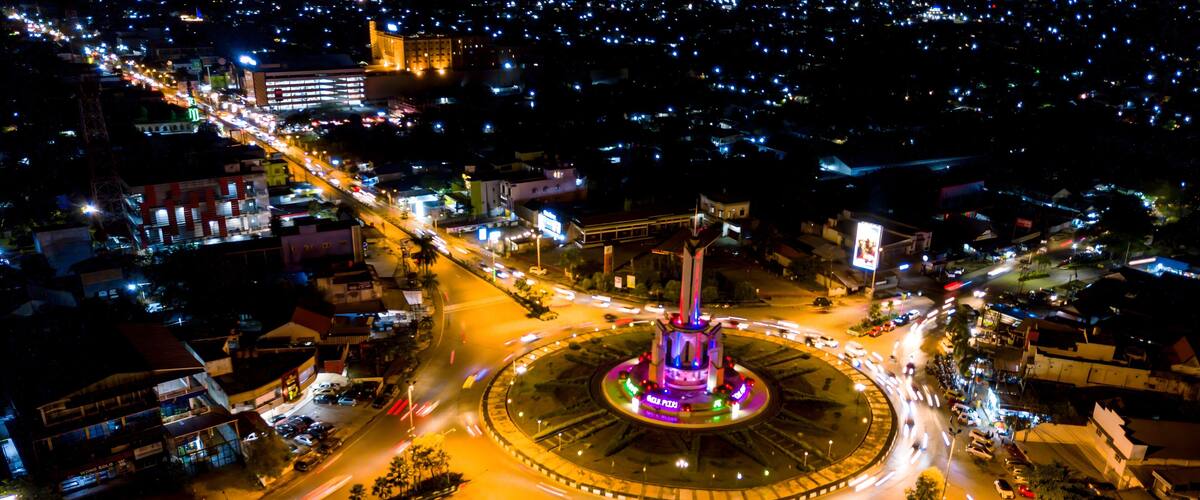 A nighttime aerial view of a city with a central roundabout, illuminated buildings, and a prominent tower.