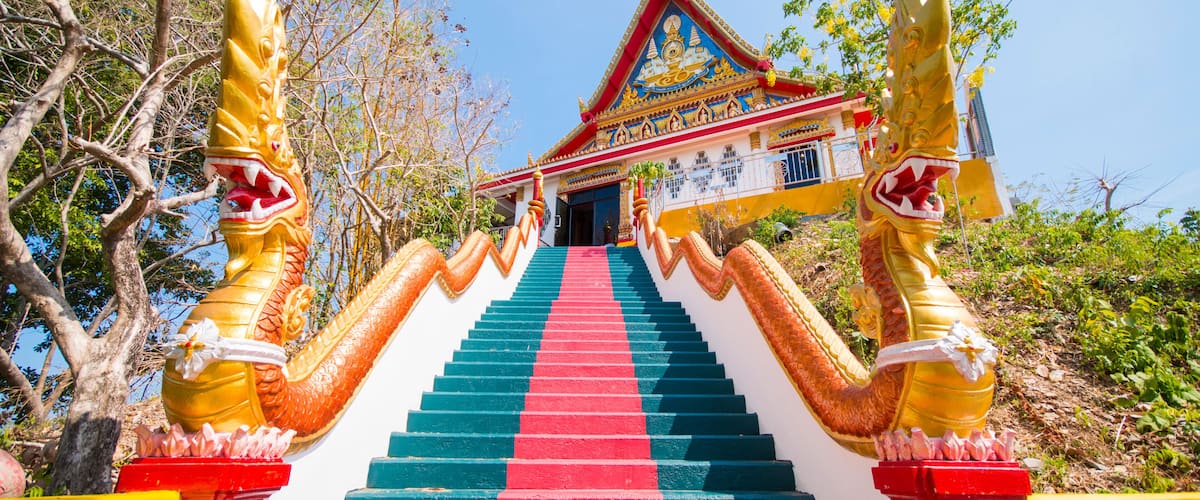 A staircase with a sign in a foreign language, leading to a temple with a colorful roof.