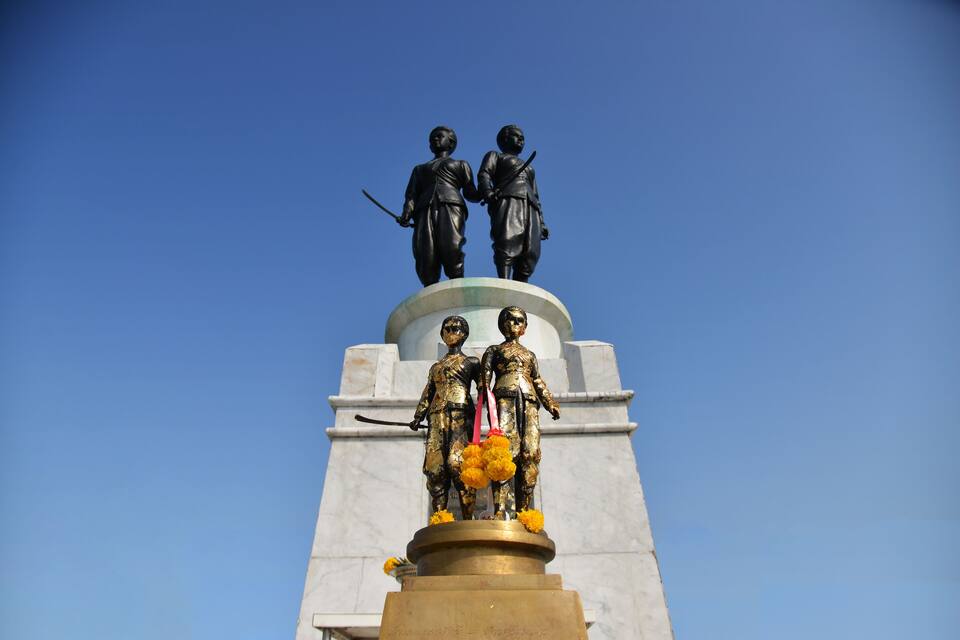 Eine Statue von zwei Figuren auf einem Sockel, im Hintergrund ein klarer, blauer Himmel.
