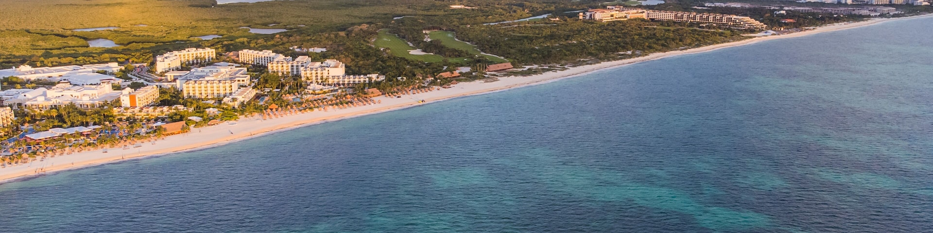 Zona turística costera con hoteles frente a la playa, una playa de arena y una extensa masa de agua.