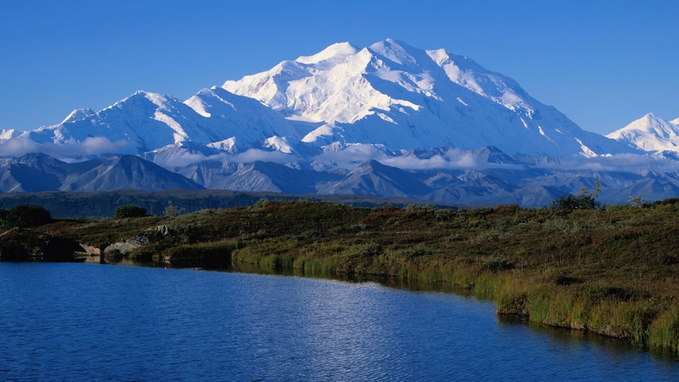 A snow-capped mountain range, a lake, and a grassy landscape.