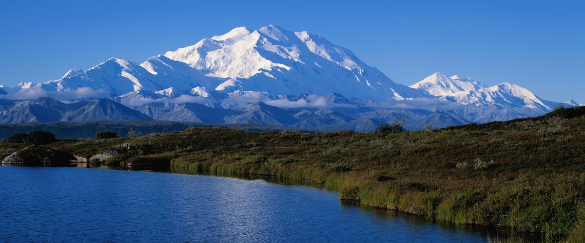 A snow-capped mountain range, a lake, and a grassy landscape.