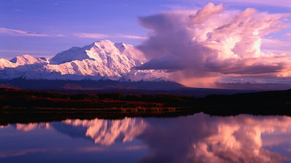 A mountain range with snow-capped peaks reflected in a calm lake.