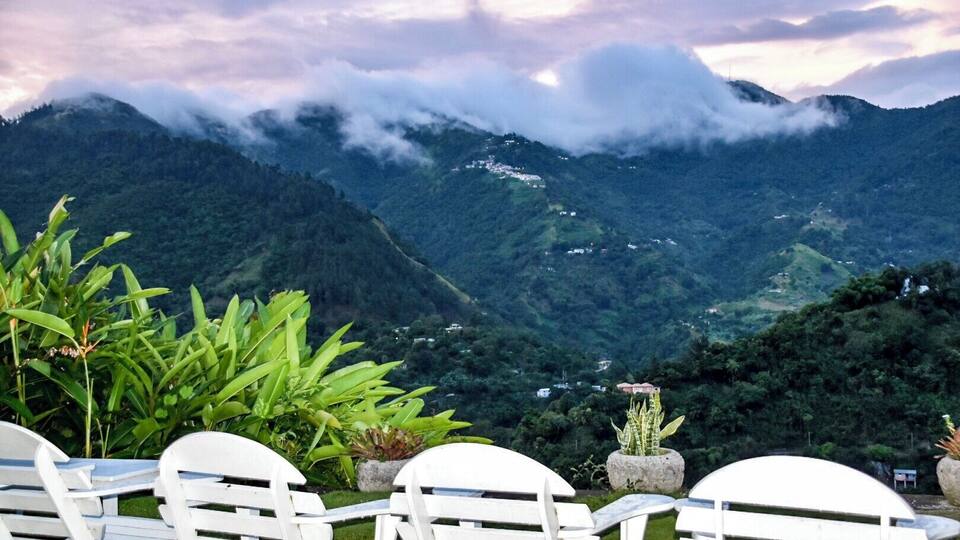 A mountainous landscape with white chairs and potted plants in the foreground.