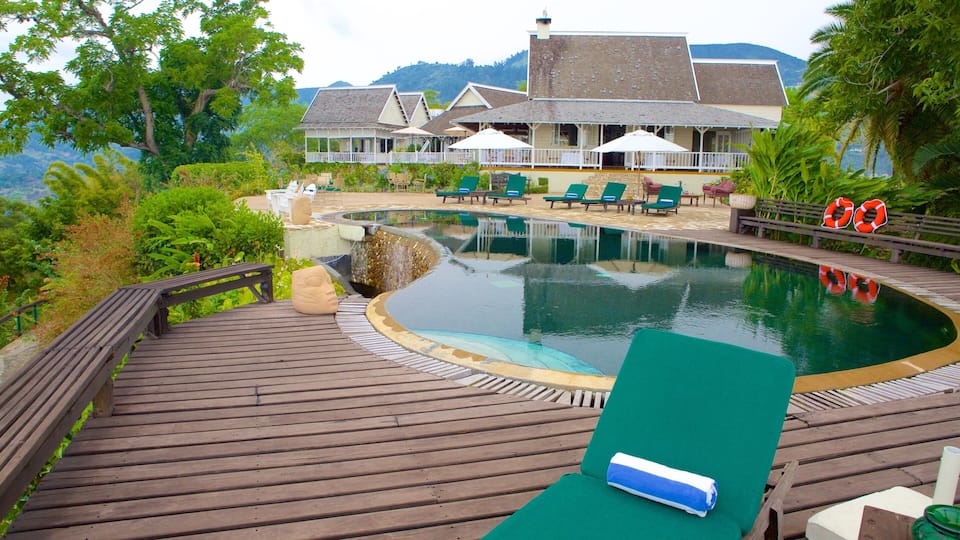 A wooden deck with a pool, lounge chairs, and a building with a balcony in the background.