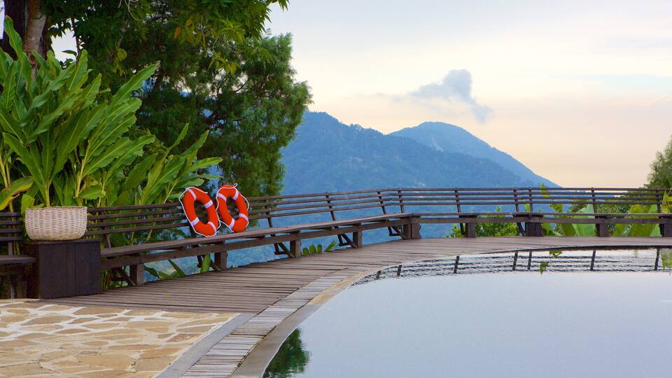 A wooden bridge over a reflective water body with lifebuoys on the railing and a mountainous backdrop.