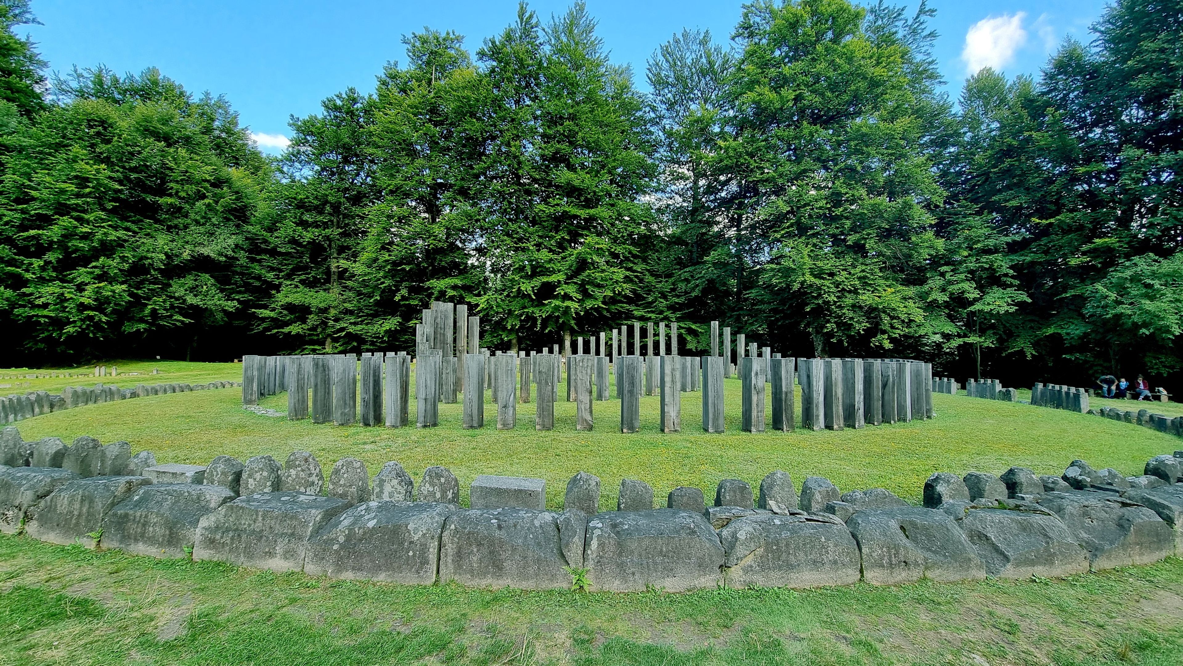 Um círculo de pedras com estacas de madeira em um campo gramado, cercado por árvores.