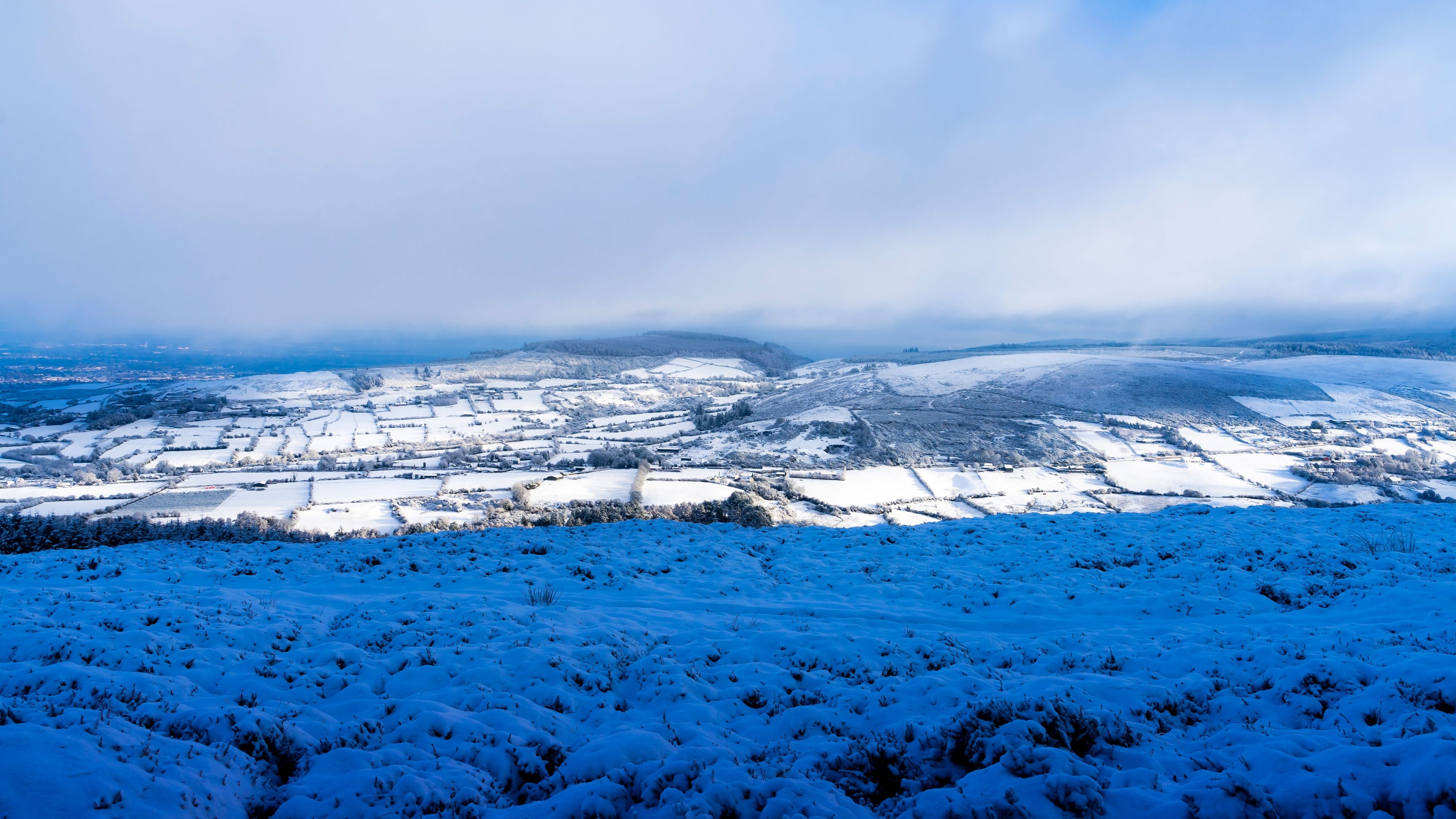 A snow-covered landscape with fields and distant hills.