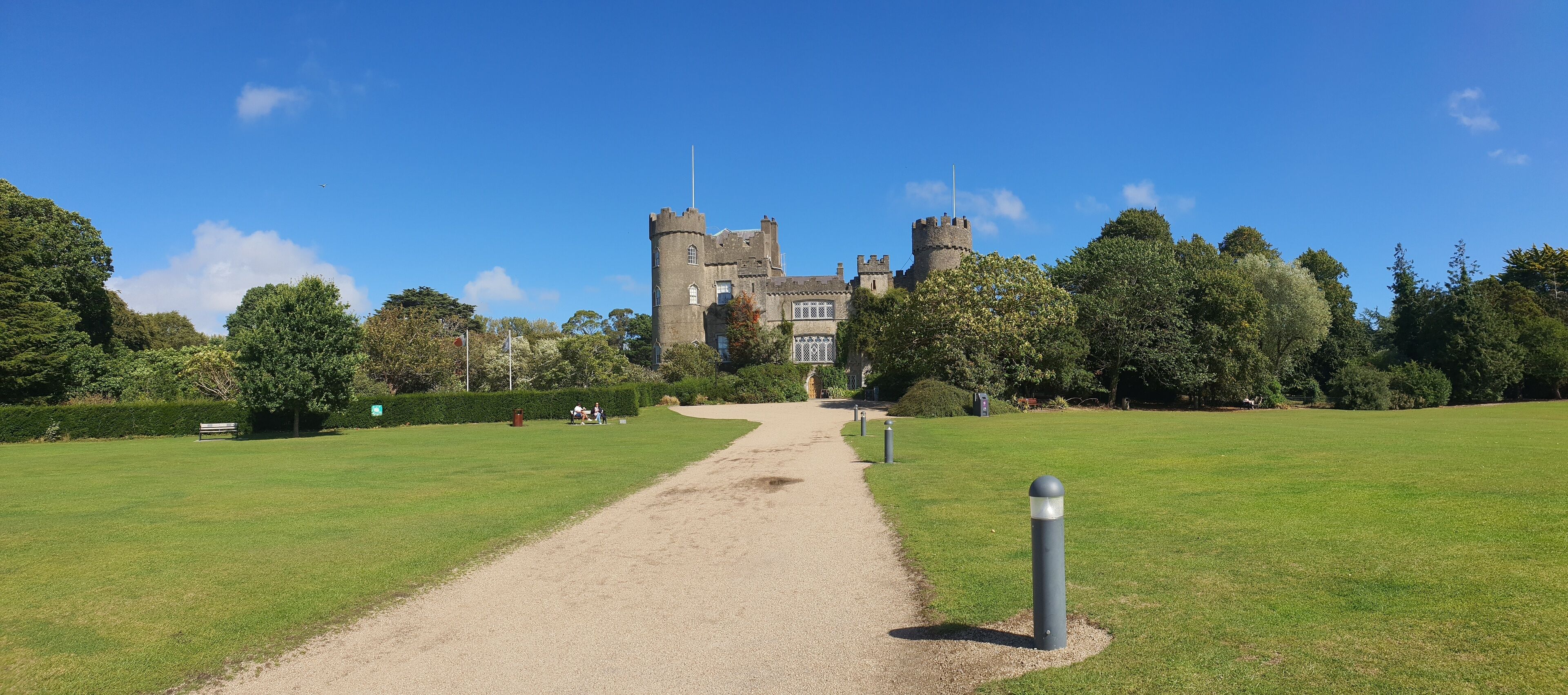 A castle with a gravel path leading to it, surrounded by green grass and trees.