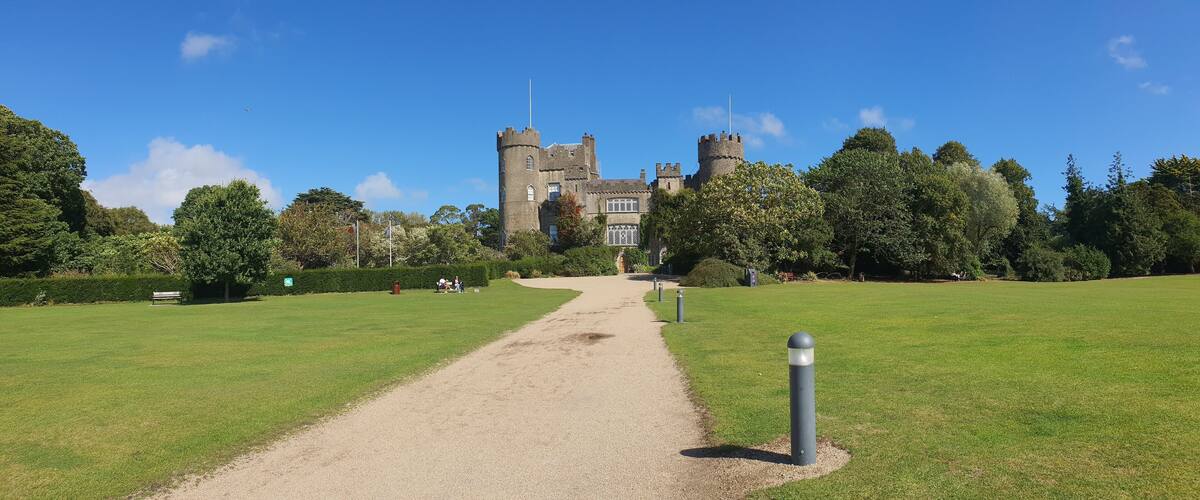 A castle with a gravel path leading to it, surrounded by green grass and trees.