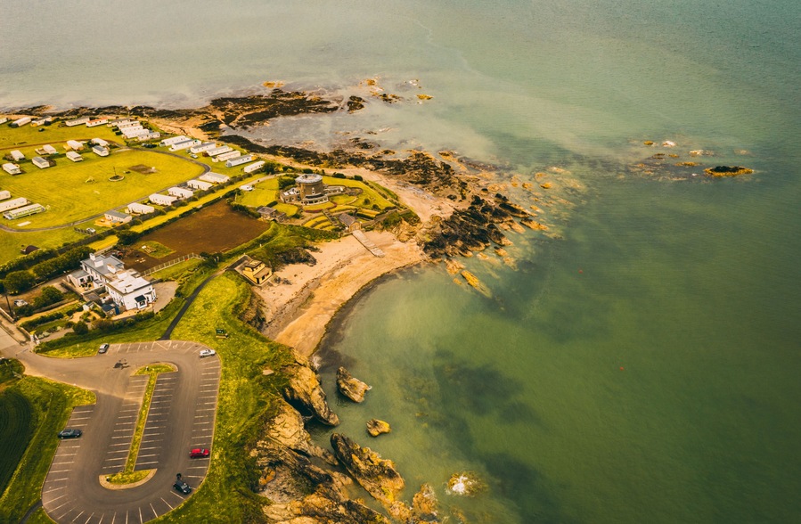 Vista aérea de uma área costeira com um porto de iates, um estacionamento e um pequeno bairro residencial.
