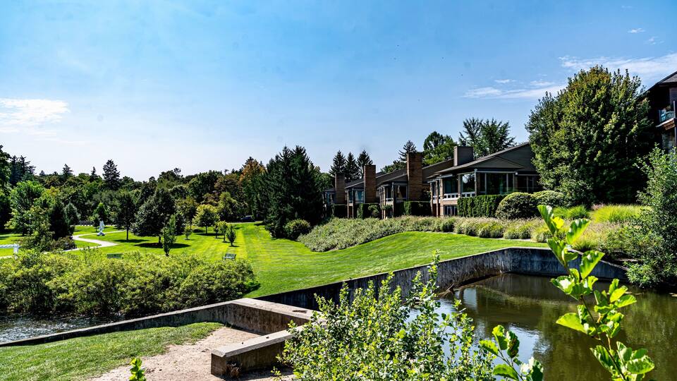A golf course with a pond, a bridge, and a building with a glass facade.