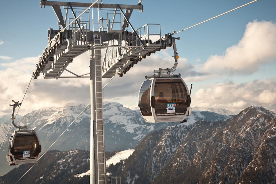 A cable car system with two cabins suspended by cables against a mountainous backdrop.