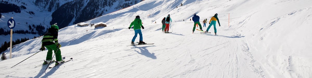 Des skieurs dévalent une pente enneigée, avec un ciel dégagé et des sommets couverts de neige en arrière-plan.