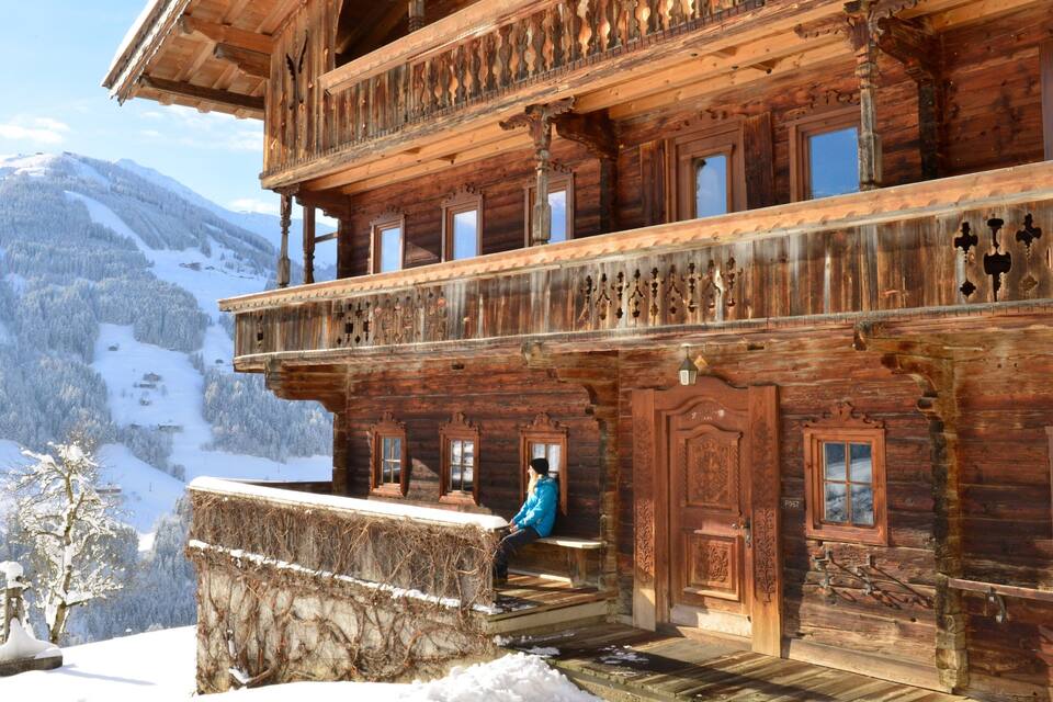 A wooden chalet with a balcony overlooking a snowy mountain landscape.
