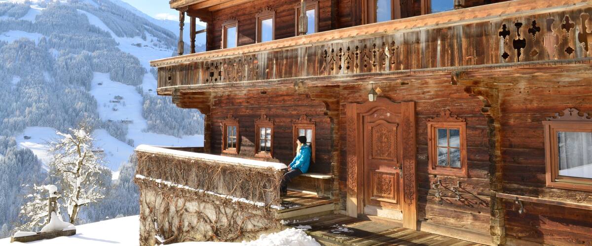 A wooden chalet with a balcony overlooking a snowy mountain landscape.