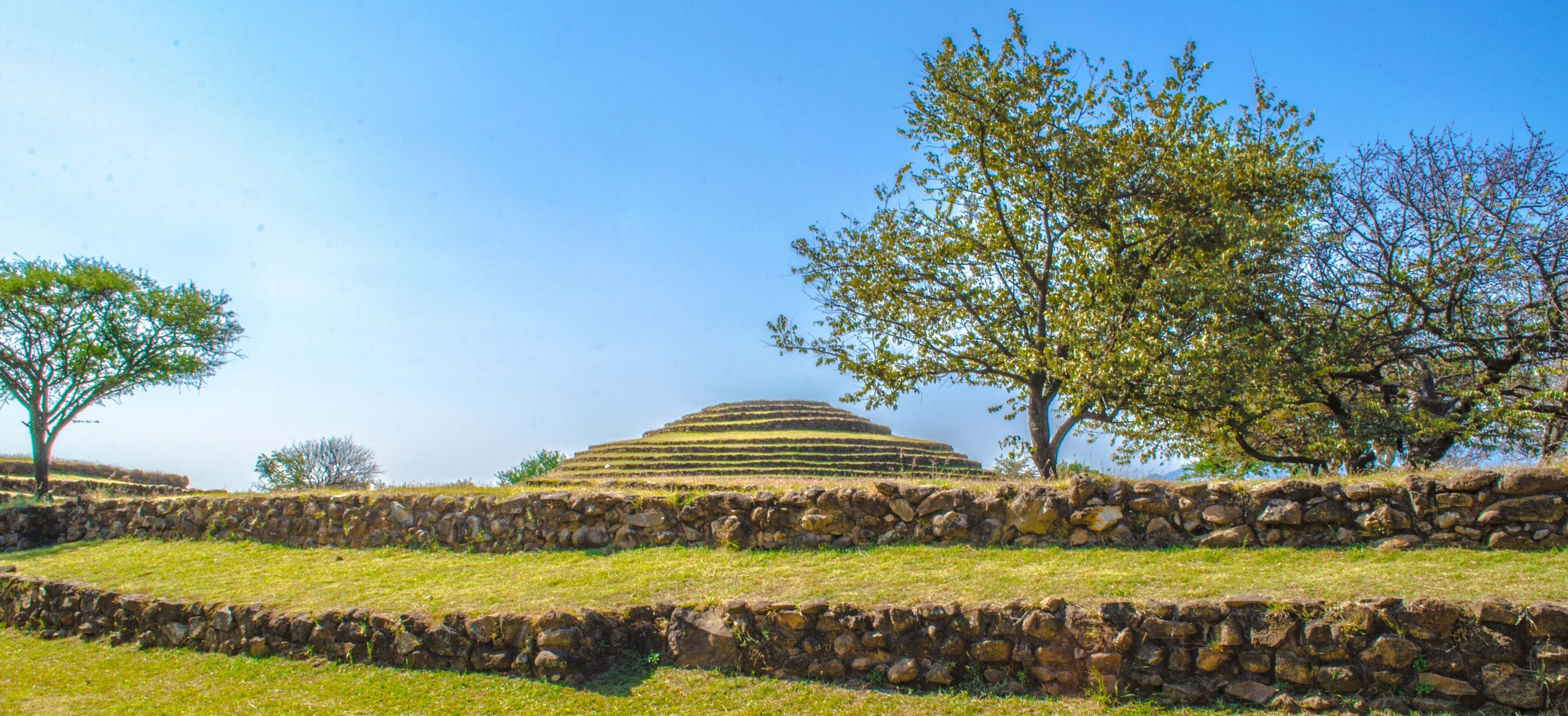 A terraced structure with stone walls and trees in a grassy field.