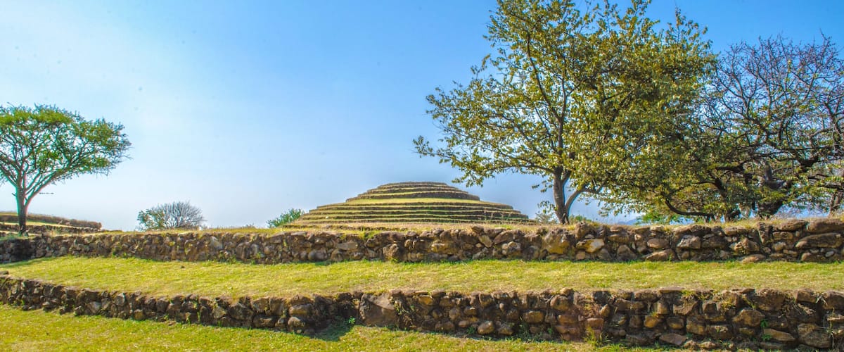 A terraced structure with stone walls and trees in a grassy field.