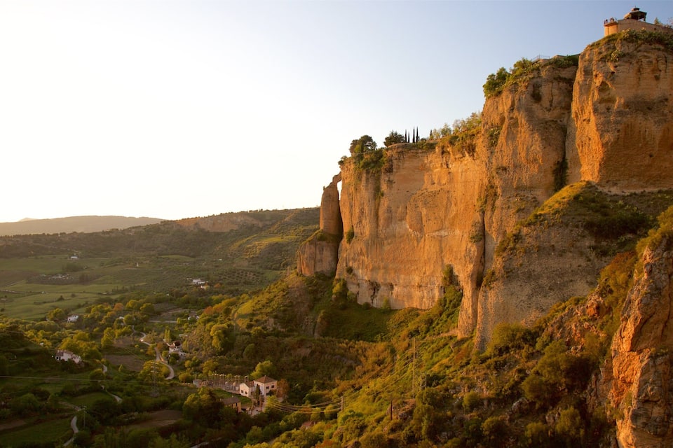 A rugged cliff with a small tower on top, surrounded by lush greenery and a valley below.