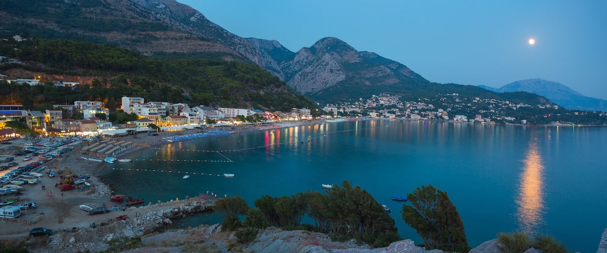 A coastal town with a marina, boats, and a mountain backdrop.