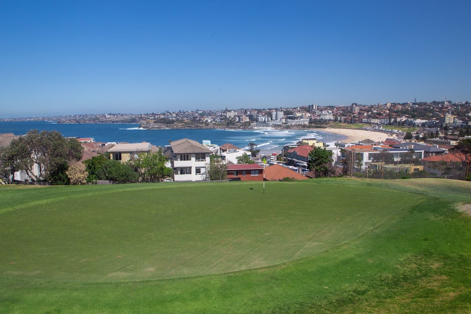 A coastal cityscape with a golf course in the foreground, beach, and ocean.
