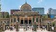 A historic building with a large dome and columns, surrounded by modern buildings and a crowd of people.