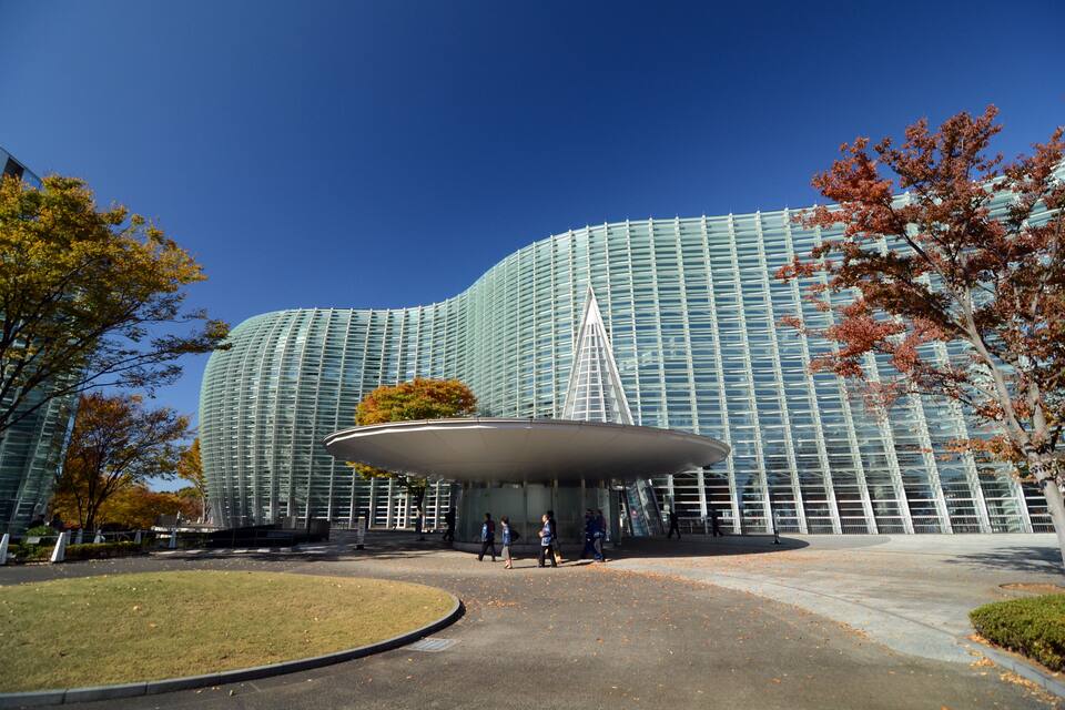 A modern glass building with a curved facade and a large, circular entrance canopy.