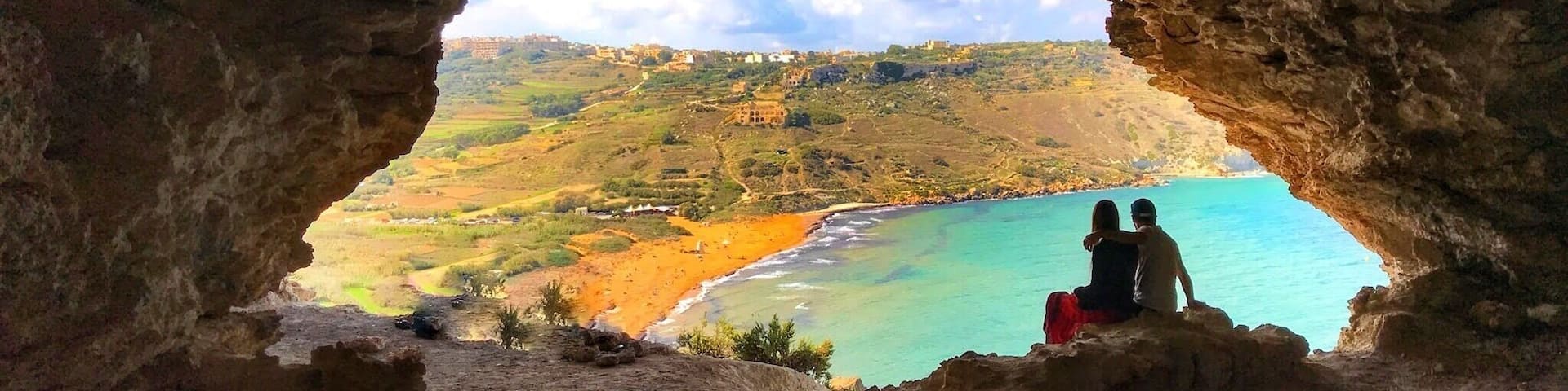 A cave opening to a coastal landscape with a view of a beach and distant hills.