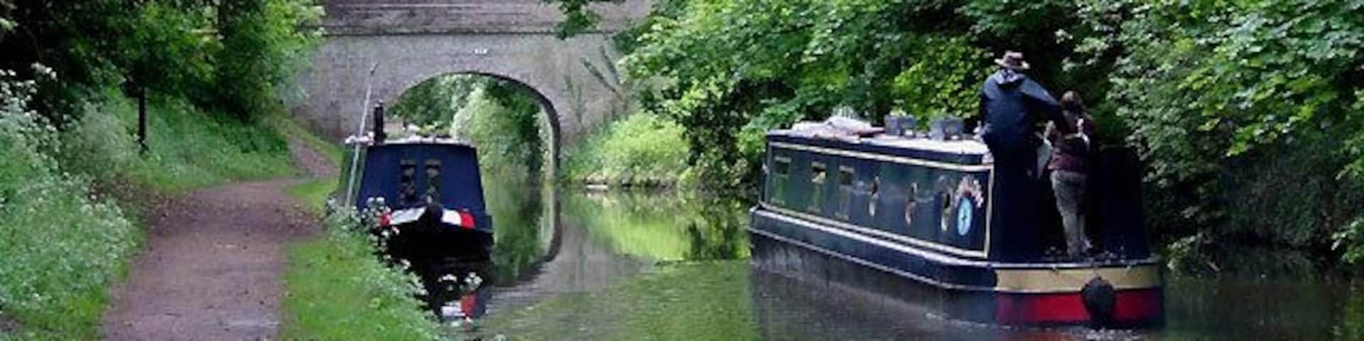 Shropshire Union Canal at Brewood, Staffordshire Narrowboat "Swallow" passes moored boats appropriately slowly as it approaches Bridge No 13, School Bridge.