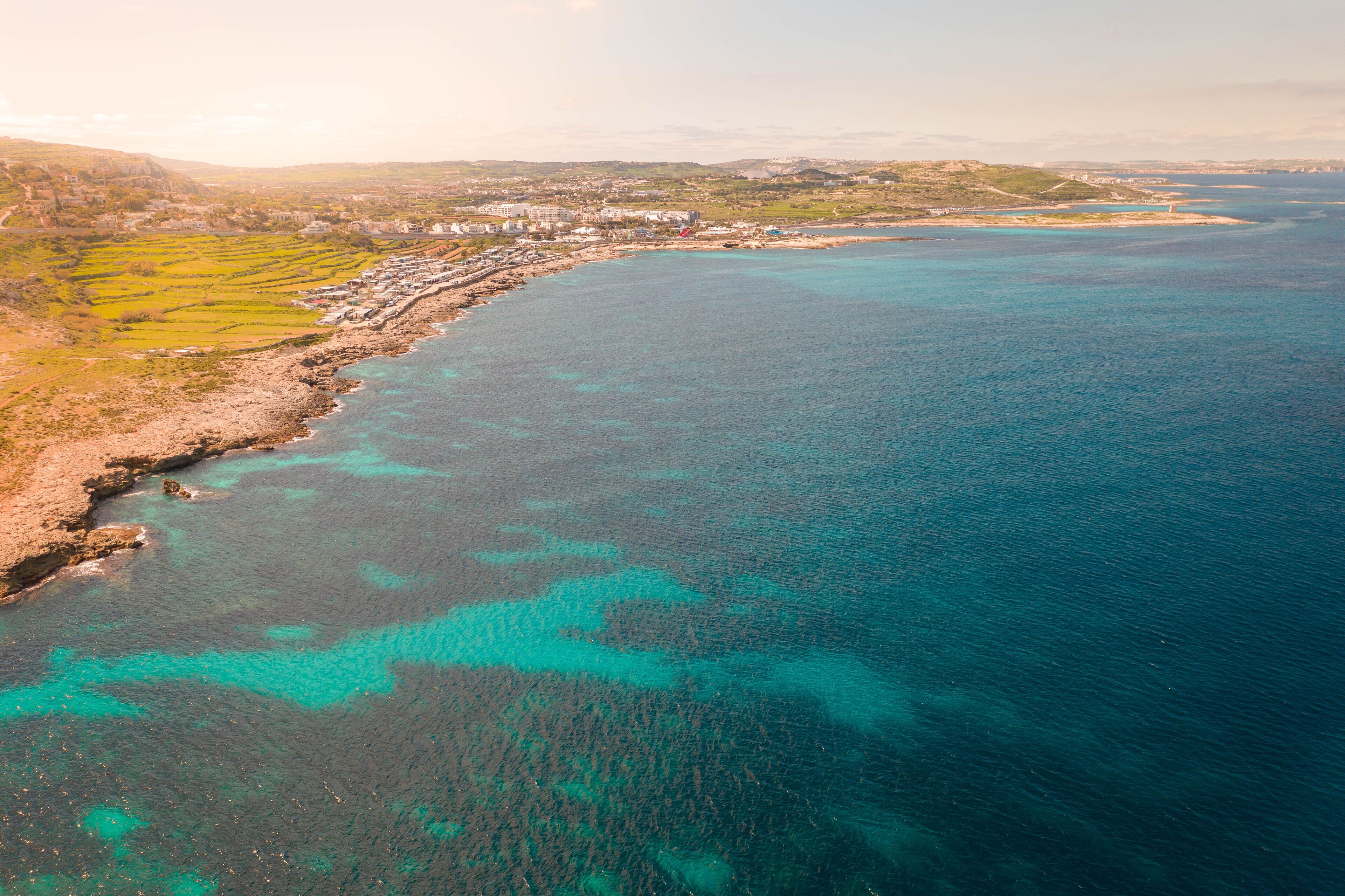 A coastal landscape with clear turquoise waters, terraced fields, and a distant town.