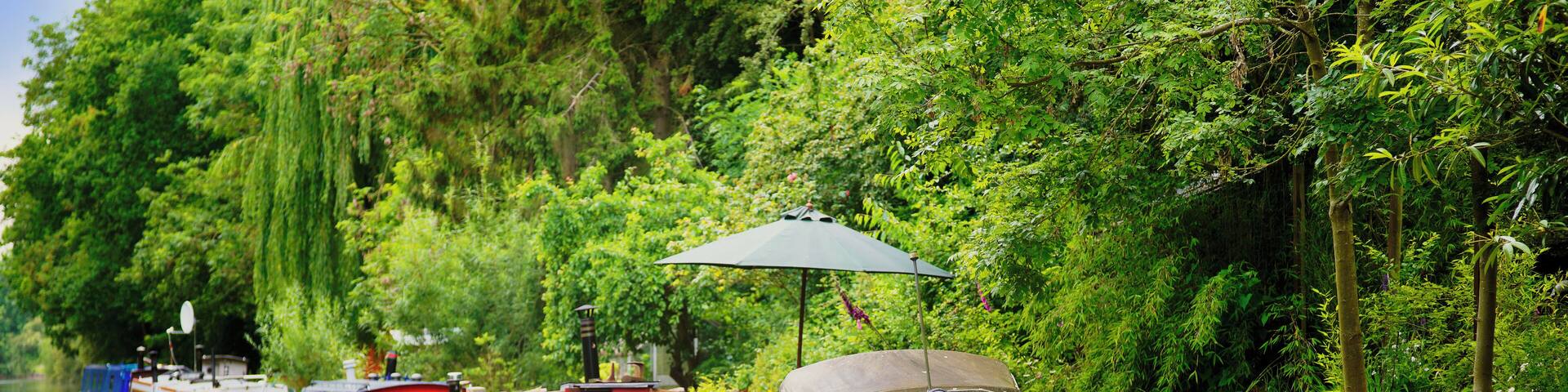 The picture shows a colourful narrow boat / barge / houseboat moored on the Grand Union Canal in Warwickshire, in the West Midlands, England, UK. It is an afternoon in summer and there is hazy sunshin