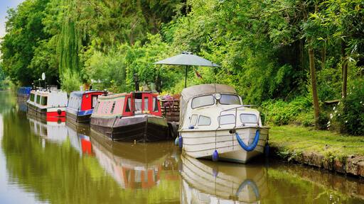 The picture shows a colourful narrow boat / barge / houseboat moored on the Grand Union Canal in Warwickshire, in the West Midlands, England, UK. It is an afternoon in summer and there is hazy sunshin