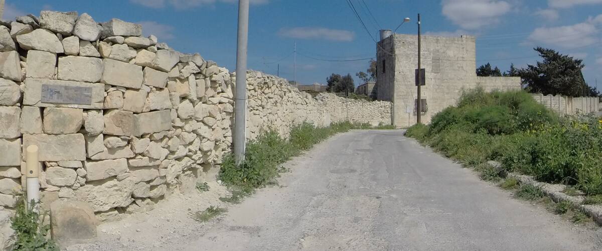 A rural road flanked by stone walls and a stone tower.